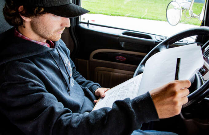 Truck driver sitting in cab of semi truck reading checklist